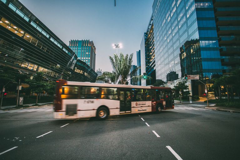 Ônibus cruzando uma avenida ao entardecer, entre prédios de vidro