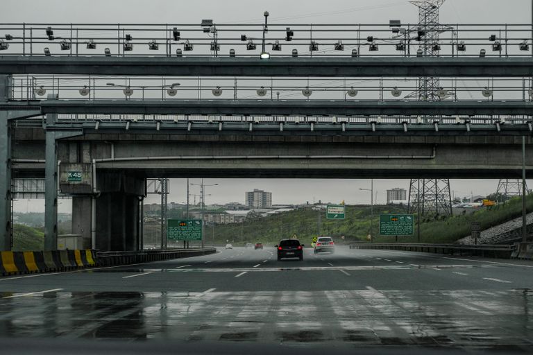 Pórtico de free flow com câmeras e sensores sobre uma rodovia de várias faixas, carros passando sem cancela
