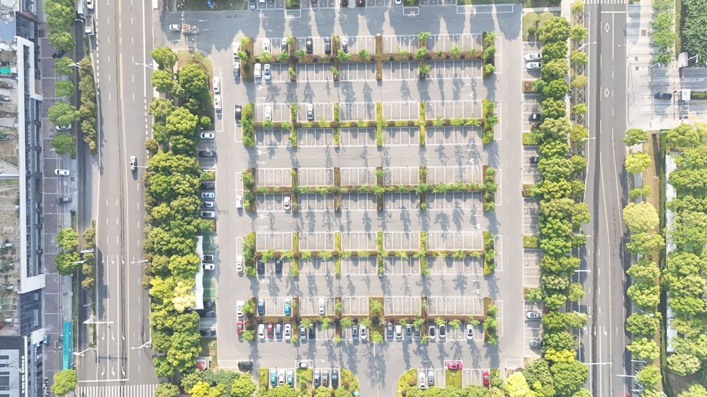 Estacionamento urbano visto de cima, com as fileiras de vagas separadas por canteiros arborizados e avenidas dos dois lados