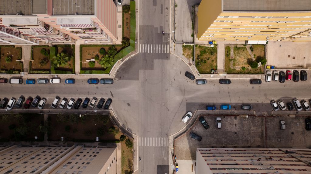 Cruzamento urbano visto de cima, com vagas na via pública perpendiculares e paralelas ao meio-fio