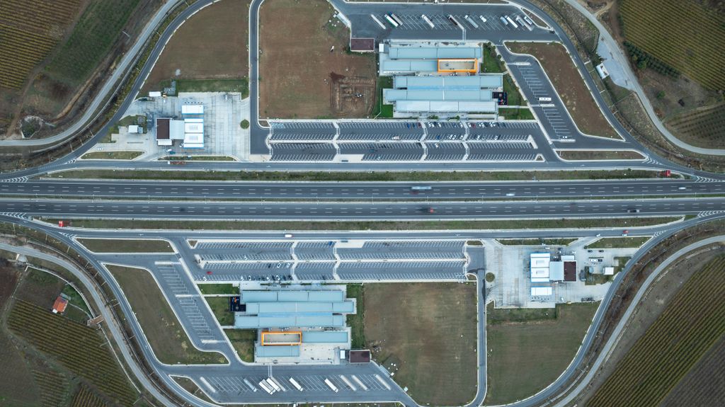 Rodovia de pista dupla vista do alto, com áreas de serviço dos dois lados ligadas à pista por alças de acesso