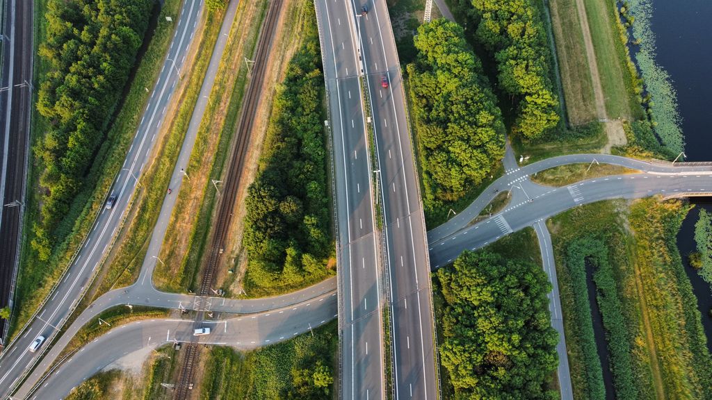 Rodovia de pista dupla vista de cima, com vias paralelas dos dois lados, a ferrovia e uma ligação que passa por baixo
