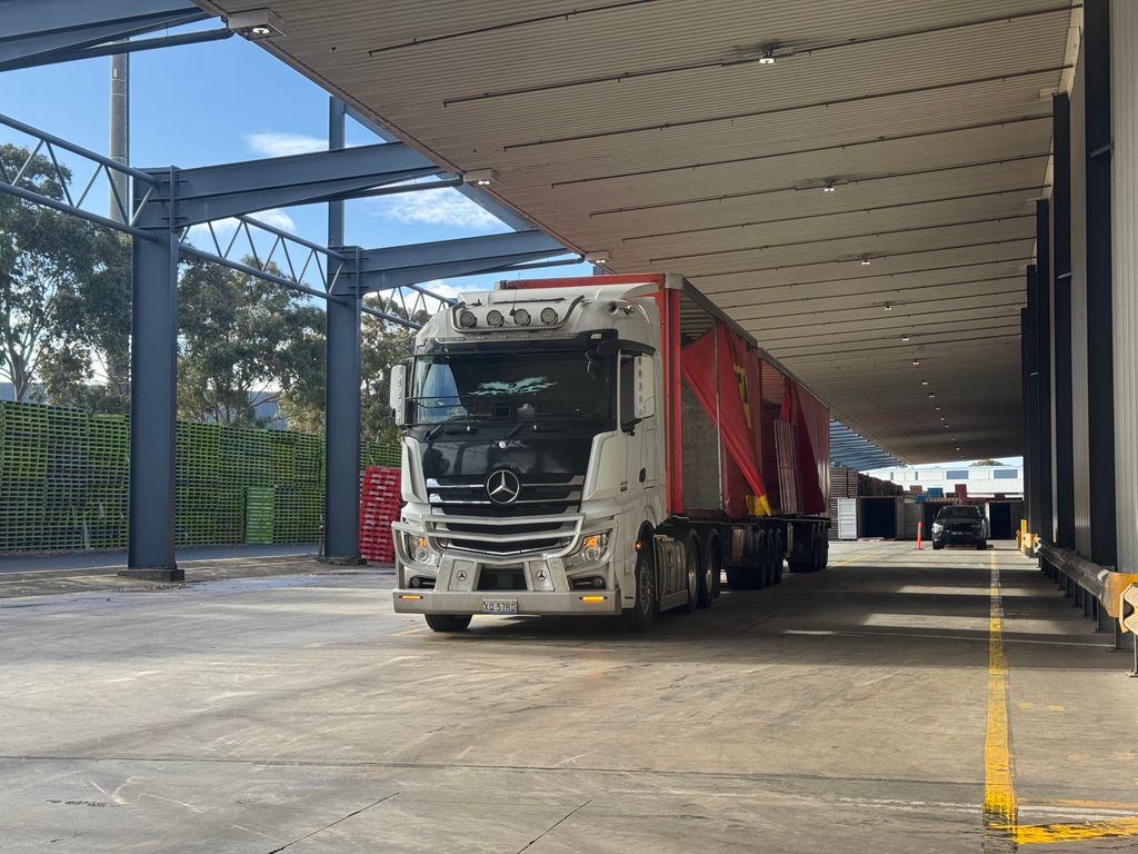 Caminhão com carreta de lona parado sob a cobertura da doca de um armazém