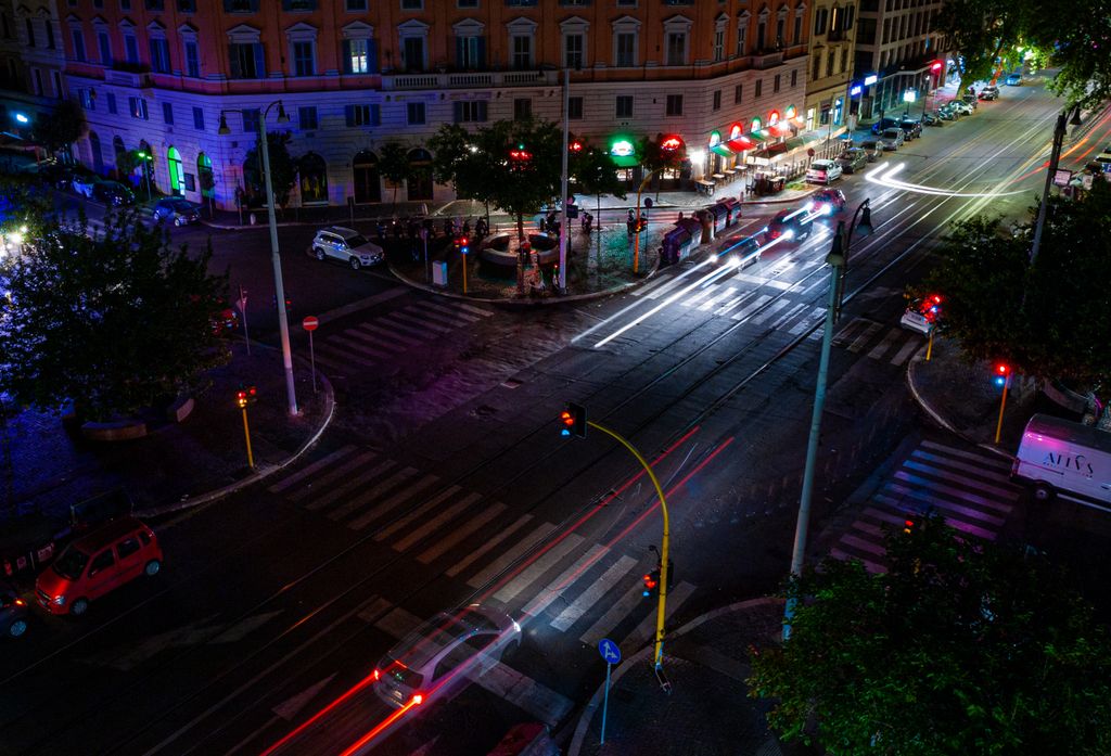 Cruzamento semaforizado à noite, visto do alto, com rastros de luz dos veículos
