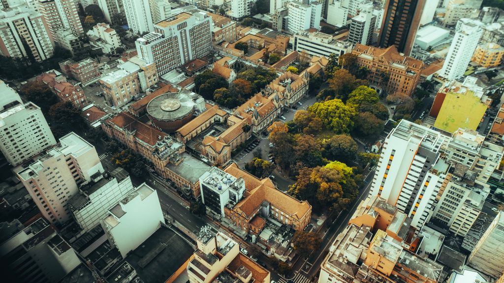 Vista aérea de um centro urbano, com prédios históricos de telhado cerâmico, uma praça arborizada e edifícios altos em volta