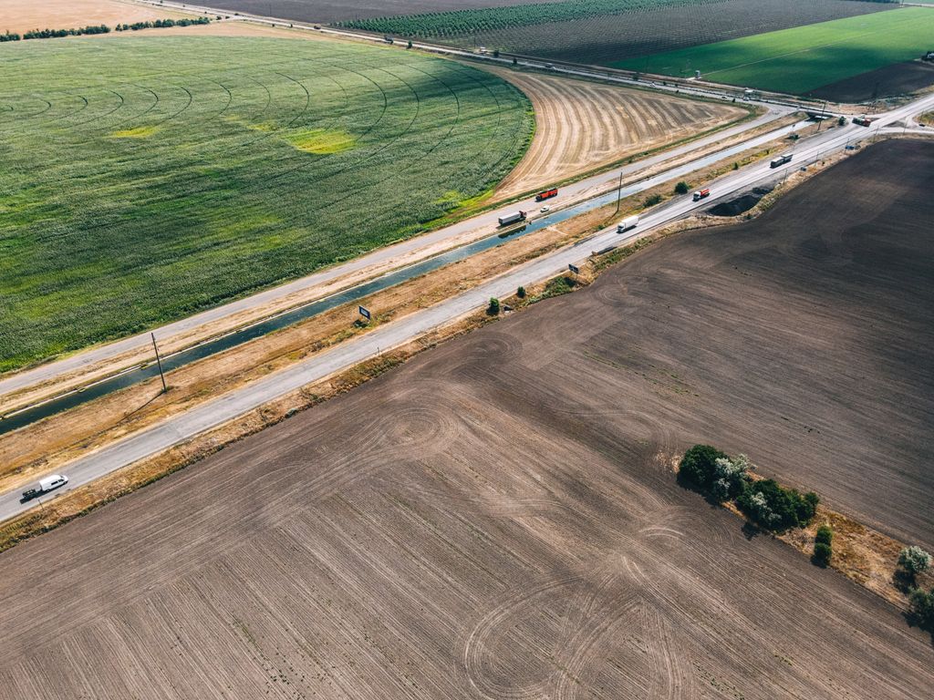 Rodovia de pista dupla entre lavouras, com caminhões, vista do alto