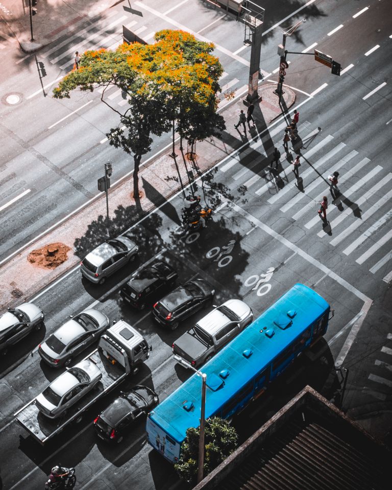 Cruzamento urbano visto do alto, com a fila de carros e um ônibus parados antes da faixa de pedestres