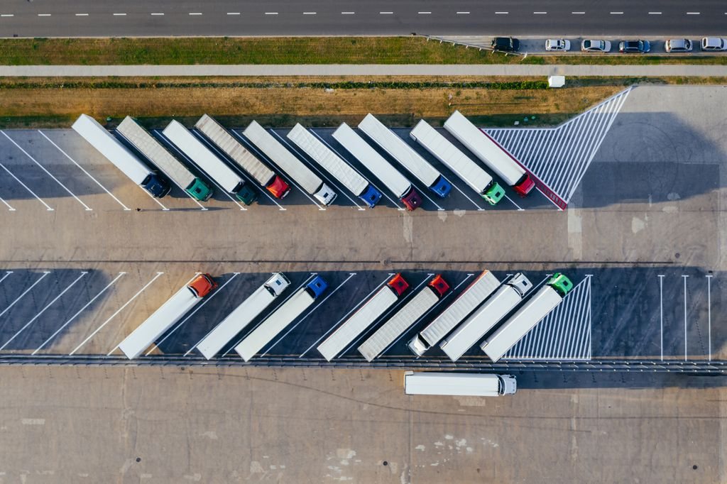 Área de descanso vista do alto, com caminhões estacionados em duas fileiras de vagas em espinha e a rodovia ao fundo