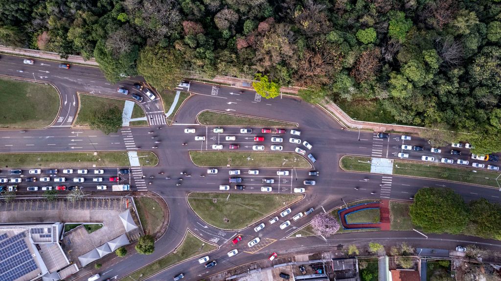 Avenida urbana de pista dupla vista de cima, com retornos, faixas de pedestre e trânsito intenso