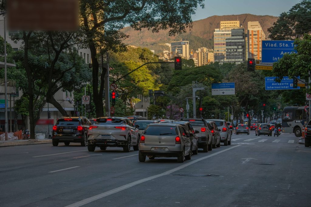 Avenida arborizada de Belo Horizonte ao entardecer, com semáforos em sequência ao longo do corredor e a serra ao fundo