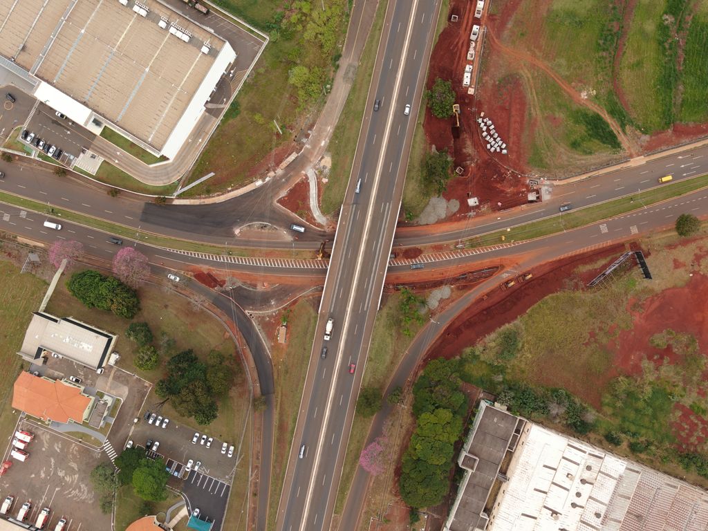 Vista aérea vertical de uma rodovia duplicada que passa em viaduto sobre uma avenida, com os ramos do trevo e a obra de ampliação ao lado