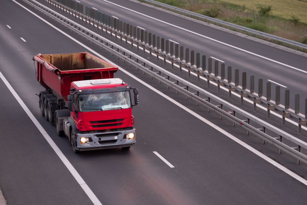 Caminhão basculante vermelho na faixa da direita de uma rodovia de pista dupla, visto do alto